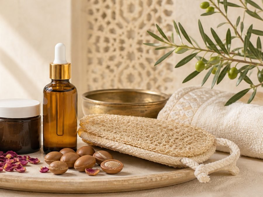 Argan oil, ghassoul clay, rose petals and a kessa glove on a wooden tray